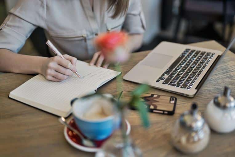 Closeup of someone writing out a content plan in a notebook in front of a laptop