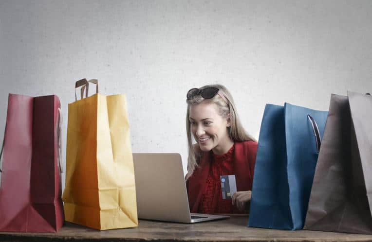 Smiling woman holding her credit card in front of her laptop surrounded by shopping bags