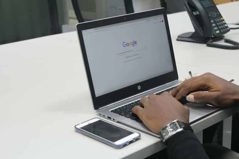 Man performing a Google search on a laptop beside his phone